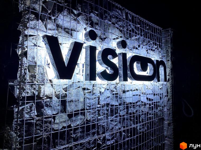 Зовнішній вигляд новобудови VISION з підсвіченими літерами на фоні кам'яної стіни. Комплекс має оригінальний дизайн фасаду.