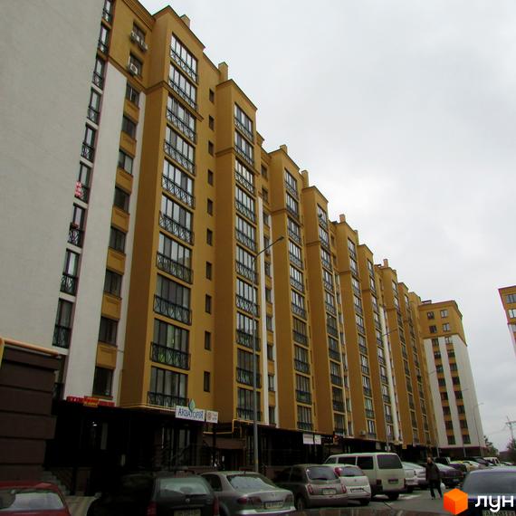 Житловий комплекс Щасливий на Петропавлівці. Фасад будинку жовтого кольору з численними вікнами та балконами. Біля будинку розташовані автомобілі.