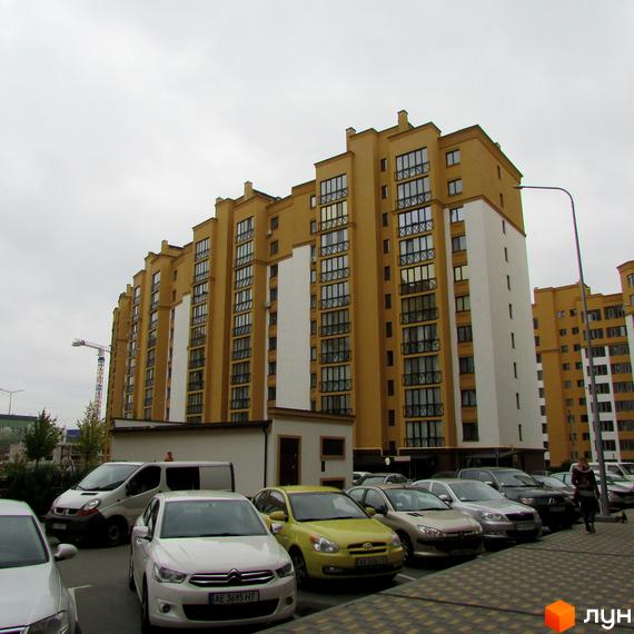 Житловий комплекс Щасливий на Петропавлівці. Зовнішній вигляд будинку з жовтою фасадною обробкою та білими вставками. Парковка з автомобілями біля новобудови.
