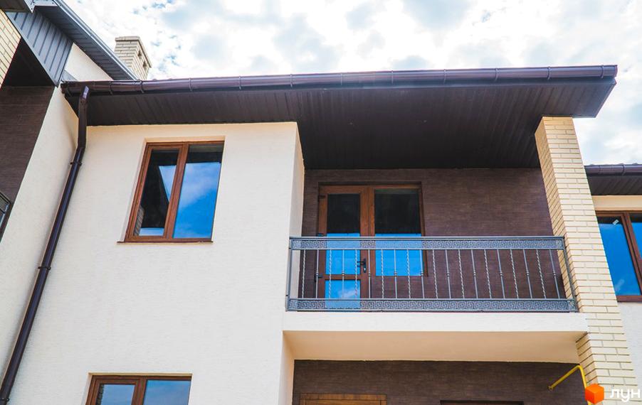 Фасад будинку ж/м «Червоний Хутір» з бежевою штукатуркою, коричневою цеглою та дерев'яними вікнами. Наявний балкон з металевими перилами.