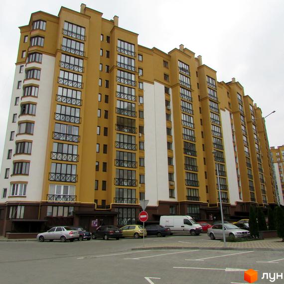 Зовнішній вигляд новобудови ЖК Щасливий на Петропавлівці. Навколо будинку розташовані автомобілі та дерева.