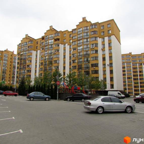 Житловий комплекс Щасливий на Петропавлівці. Зовнішній вигляд фасаду будинку та прибудинкова територія з парковкою та дитячим майданчиком.