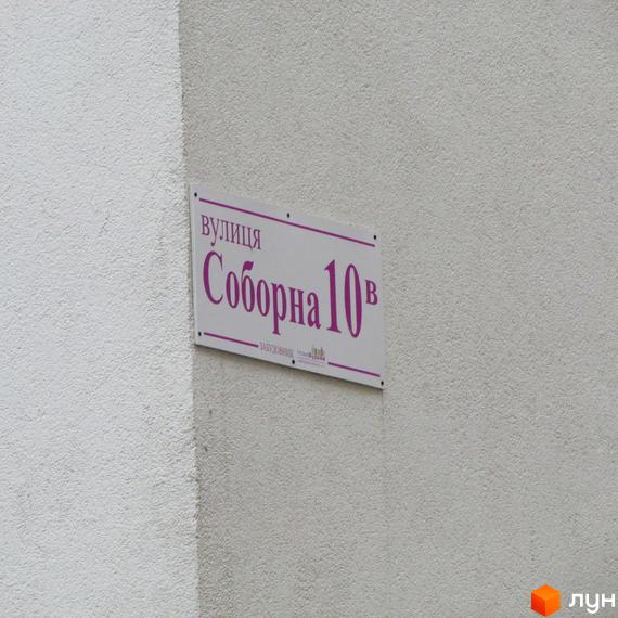 Вулична табличка з назвою вулиці Соборна 10В. Напис виконаний фіолетовим кольором на білому фоні. Напис