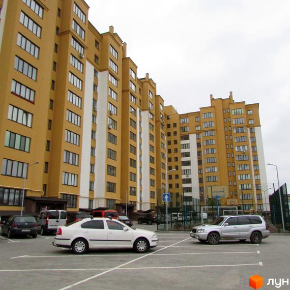 Житловий комплекс Щасливий на Петропавлівці. Фасад будинку жовтого кольору з білими вставками, паркінг з автомобілями.