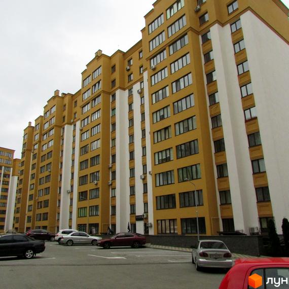 Житловий комплекс Щасливий на Петропавлівці з жовто-білими фасадами та численними вікнами. Поруч розташований паркінг з автомобілями.