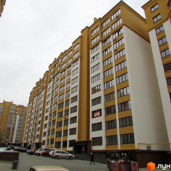 Житловий комплекс Щасливий на Петропавлівці – багатоповерхова будівля з жовто-білим фасадом. Перед будинком розташована парковка з автомобілями.