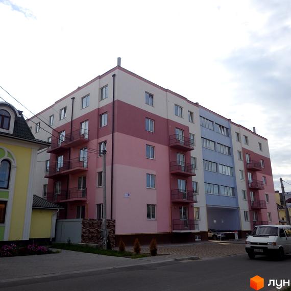 Житловий комплекс Твій дім - це багатоповерховий будинок з балконами та вікнами, пофарбований у рожеві та блакитні кольори. Прибудинкова територія облаштована тротуаром та зеленими насадженнями.