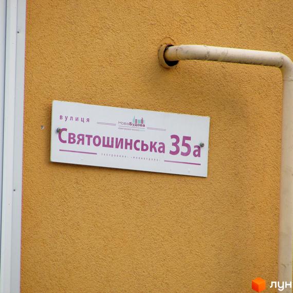 Вулична табличка новобудови Святошинська 35а на жовтому фасаді будівлі. Зовнішній вигляд фасаду та таблички.