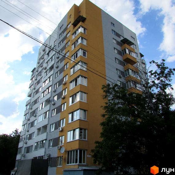 Житловий комплекс Щасливий у Вишневому: багатоповерховий будинок з жовто-сірим фасадом, вікнами та кондиціонерами. Поруч дерева та блакитне небо з хмарами.