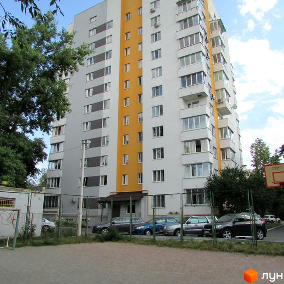 Зовнішній вигляд багатоповерхового будинку ЖК Щасливий у Вишневому з жовто-сірими фасадами. На прибудинковій території видно паркування автомобілів та спортивний майданчик.