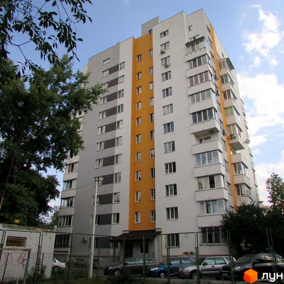 Житловий комплекс Щасливий у Вишневому – багатоповерховий будинок з жовто-сірим фасадом та балконами. Навколо будинку розташована прибудинкова територія із зеленими насадженнями та парканом.