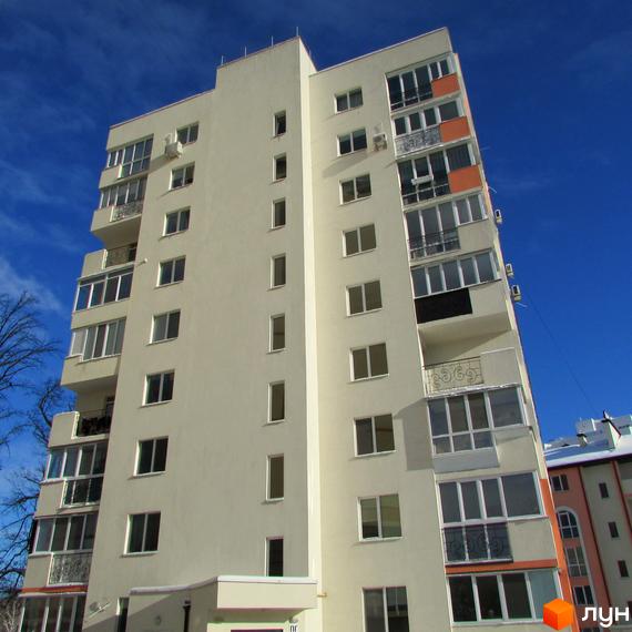 Зовнішній вигляд багатоповерхового будинку ЖК Квітневий під яскравим блакитним небом. Будинок має світлий фасад та численні вікна, деякі з яких засклені балкони.