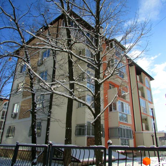 Зовнішній вигляд новобудови ЖК Квітневий у зимовий період. Фасад будинку світло-бежевий з помаранчевими елементами, багато вікон та балконів. Навколо ростуть дерева, вкриті снігом.