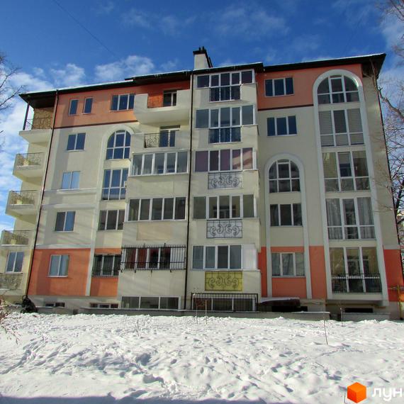 Житловий комплекс Квітневий: багатоповерховий будинок з балконами та великими вікнами на тлі блакитного неба. Прибудинкова територія вкрита снігом.