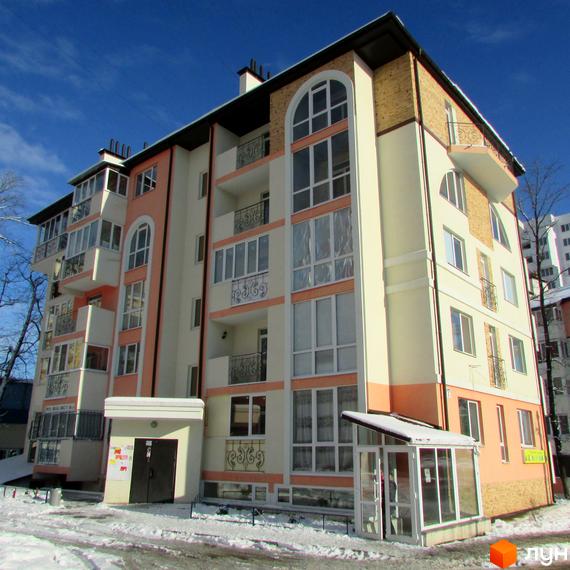 Житловий комплекс Квітневий – багатоповерховий будинок з балконами та арочними вікнами на тлі блакитного неба. Навколо будинку видно сніг та дерева.