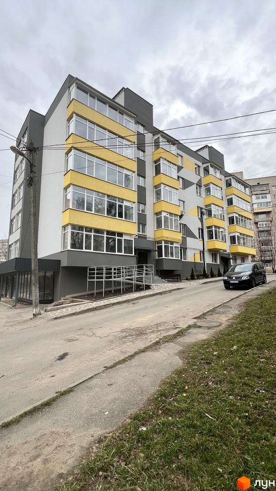 Зображення фасаду будинку на вулиці Польова, 8. Багатоповерхова будівля з жовтими балконами та сірою обробкою, поруч дорога та зелена зона.