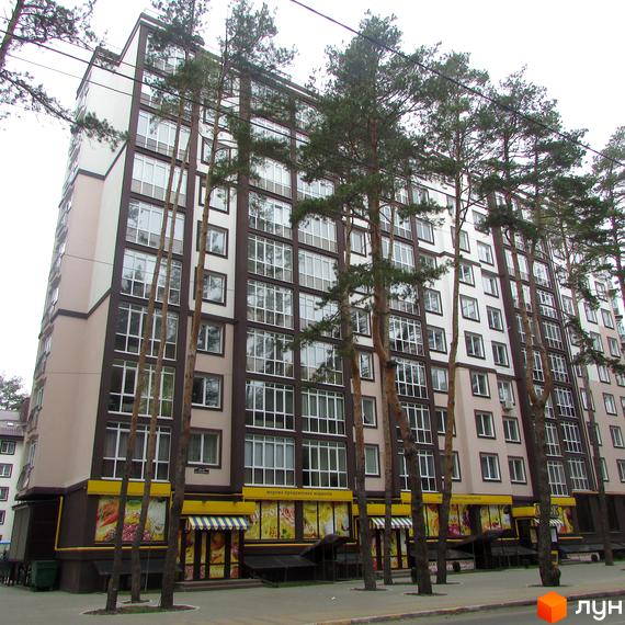 Новобудова ЖК Парковий. Багатоповерховий будинок з коричневими та білими фасадами, великою кількістю вікон та зеленими деревами на фоні.