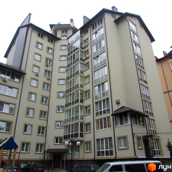 Житловий комплекс Парковий. Зовнішній вигляд багатоповерхового будинку з великою кількістю вікон та скляних балконів. На передньому плані видно елементи дитячого майданчика.