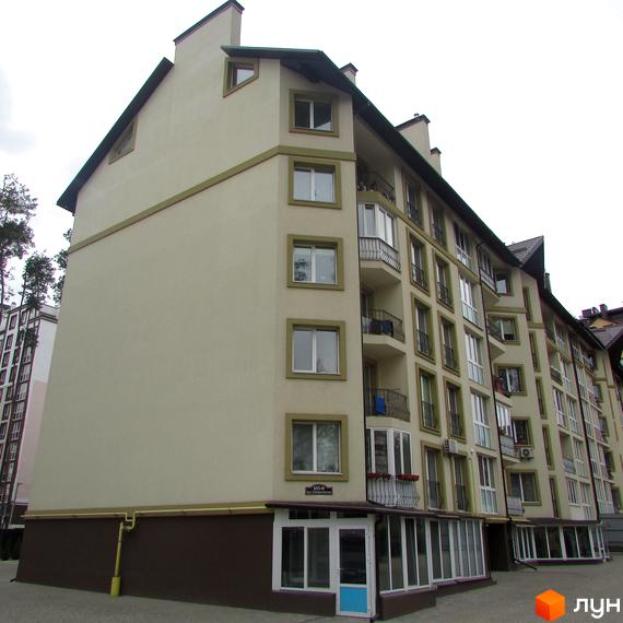 Зовнішній вигляд житлового комплексу Парковий. Багатоповерховий будинок світло-бежевого кольору з темним дахом та коричневим цоколем. Балкони з кованими огорожами.