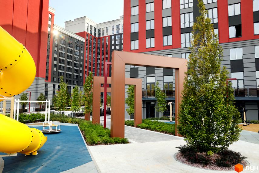 Зображення фасаду та прибудинкової території Житлового комплексу Irpin City. На фото дитячий майданчик, зелені насадження та багатоповерхівки.