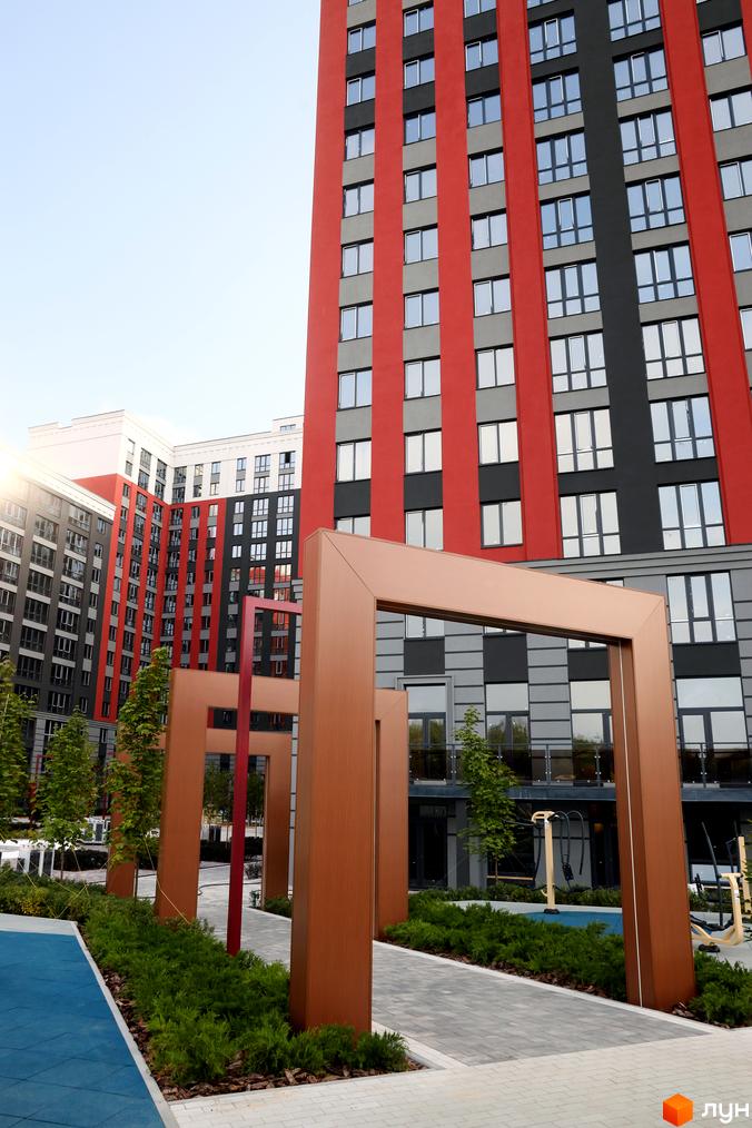 Фото фасаду і двору Житлового комплексу Irpin City. Багатоповерхова будівля з червоними смугами, дитячий майданчик та ландшафтний дизайн.