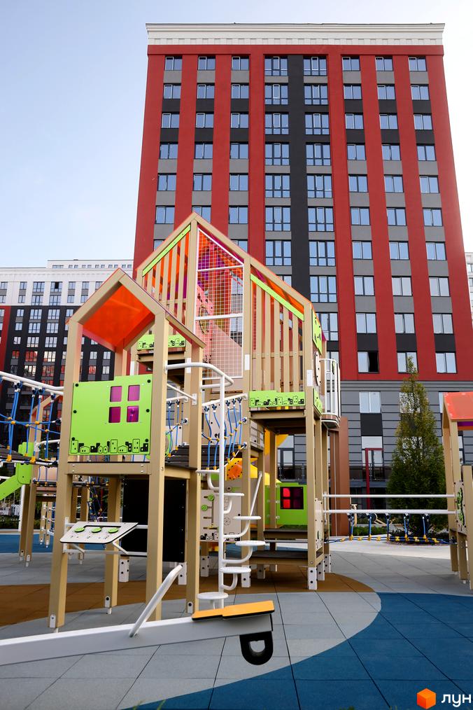 Зображення будинку та дитячого майданчика в Житловому комплексі Irpin City. Багатоповерхівка з червоним фасадом, великий ігровий комплекс.