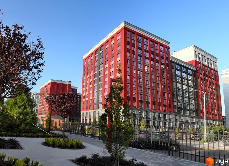 Сучасний житловий комплекс Irpin City з червоно-сірими фасадами та доглянутою прибудинковою територією з деревами та доріжками.