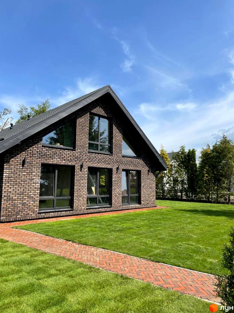 Цегляний будинок з великими вікнами на тлі блакитного неба. Доглянутий газон та доріжка з бруківки додають затишку Котеджному містечку Бельгійське село.