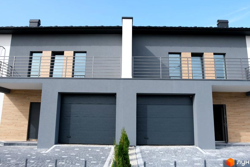 Фасад житлового комплексу на вул. Молодіжна: сірі стіни, балкони, гаражні ворота та брукований двір.