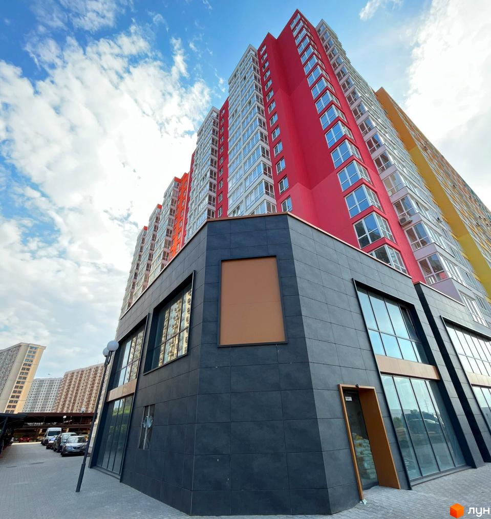 Висотна новобудова ЖК Акварель-2 з яскравим фасадом. Біля будинку розташована асфальтована територія з місцями для паркування.