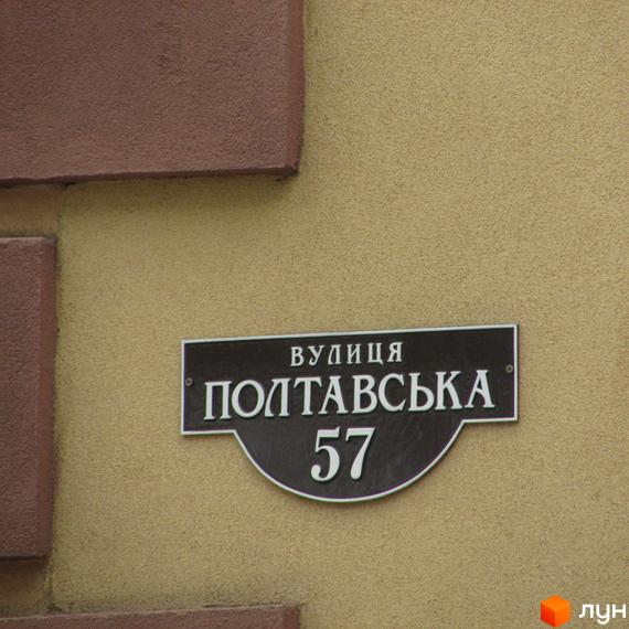 Вуличний знак з назвою вулиці Полтавська та номером будинку 57. На фоні - стіна будинку.