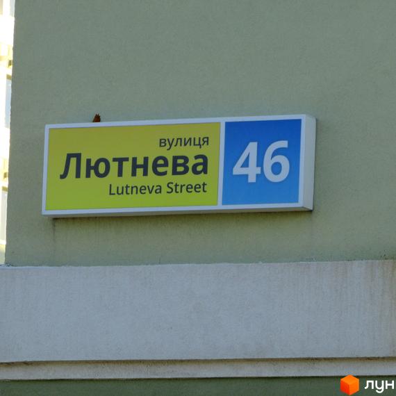 Вуличний знак з написом «Лютнева Street» та номером будинку 46. Житловий комплекс розташований на вулиці Лютнева.