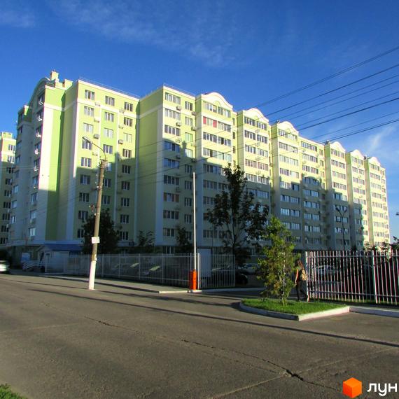 Житловий комплекс Первоцвіт. Багатоповерховий будинок з великою кількістю вікон. На території є паркан та зелені насадження.