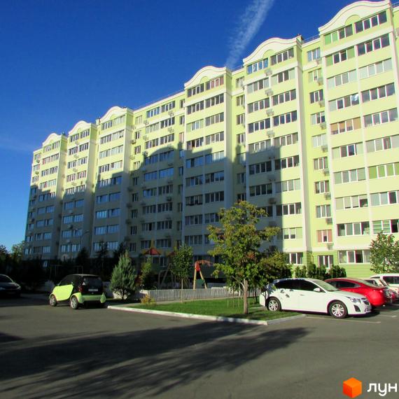 Висотна новобудова ЖК Первоцвіт з великою кількістю вікон. На прибудинковій території є парковка та дитячий майданчик.