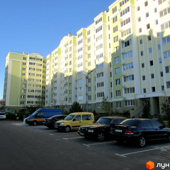 Житловий комплекс Первоцвіт з парковкою для автомобілів. Багатоповерховий будинок з великою кількістю вікон, пофарбований у світлі кольори.