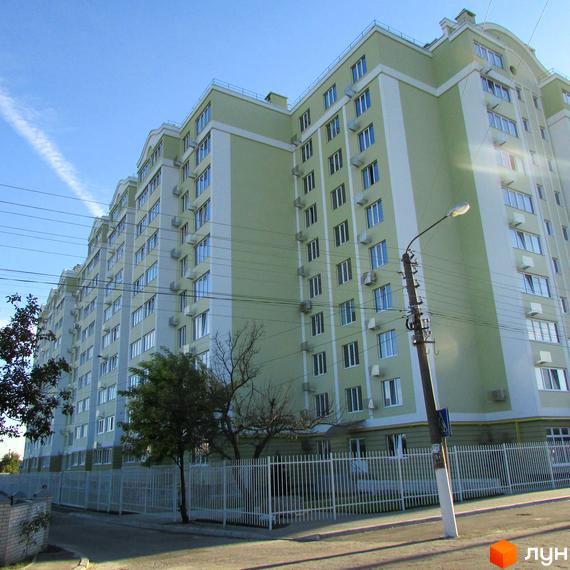 Висотна будівля житлового комплексу Первоцвіт з великою кількістю вікон. Перед будинком розташована прибудинкова територія з огорожею та деревами.