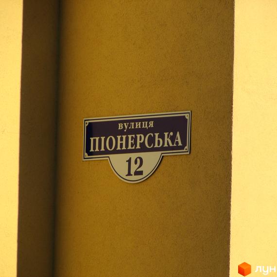 Вивіска вулиці Піонерська 12 на жовтому фоні. Зображення показує частину будівлі з вказівником адреси.