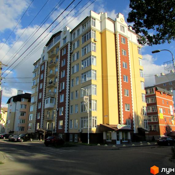 Висотна будівля житлового комплексу Екофлетс з великою кількістю вікон. На передньому плані видно прибудинкову територію з автомобілями.