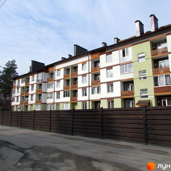 Зображення житлового будинку ЖК Європейський з балконами та вікнами. Перед будинком розташований дерев'яний паркан та асфальтована дорога.