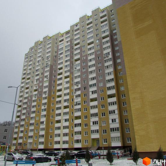 Висотна будівля житлового комплексу Ярославичі з великою кількістю вікон. На прибудинковій території видно парковку з автомобілями та невеликі кущі.