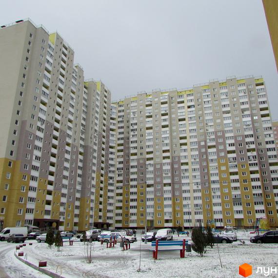 Високоповерховий житловий комплекс Ярославичі з великою кількістю вікон та балконів. На прибудинковій території є місця для паркування автомобілів, лавочки та дерева.