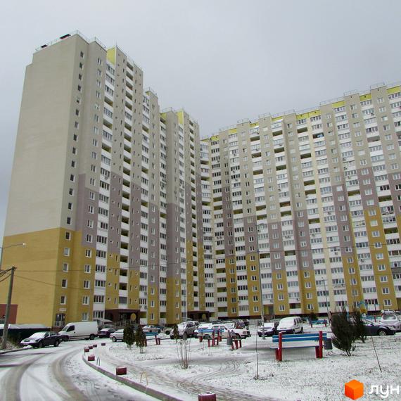 Високоповерховий житловий комплекс Ярославичі з великою кількістю вікон. На прибудинковій території є парковка та сніг.