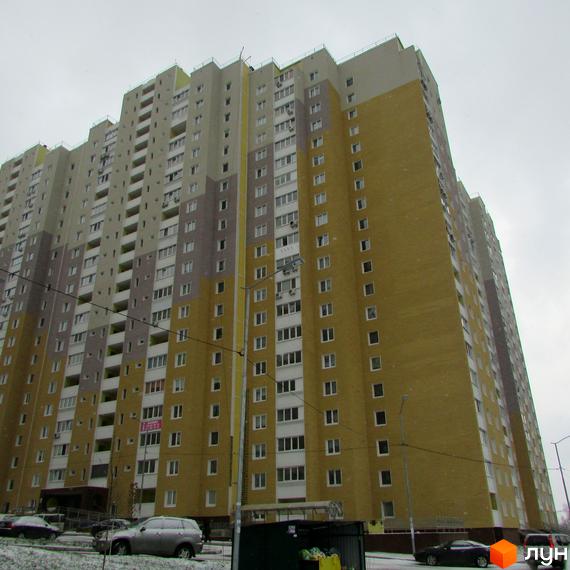 Високий будинок житлового комплексу Ярославичі з великою кількістю вікон. На передньому плані припарковані автомобілі та сміттєвий бак.