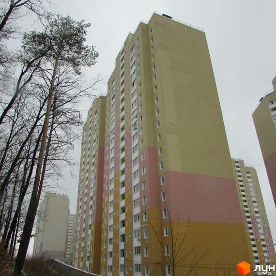 Багатоповерховий будинок житлового комплексу Ярославичі. Фасад будівлі виконаний у світлих тонах. На передньому плані дерева.