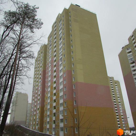 Висотна будівля ЖК Ярославичі з фасадом у світлих тонах. На передньому плані дерева, а на задньому - інші будинки комплексу.