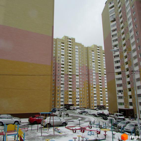 Житловий комплекс Ярославичі. Високі багатоповерхові будинки з великою кількістю вікон. На території є дитячий майданчик та парковка для автомобілів, вкрита снігом.