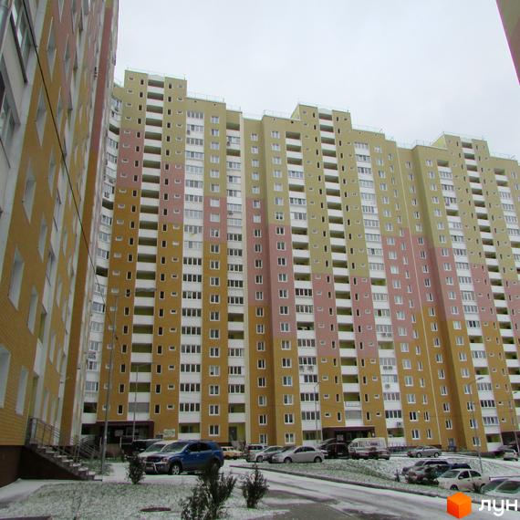 Висотна будівля ЖК Ярославичі з великою кількістю вікон та балконів. На прибудинковій території розташована парковка для автомобілів, трохи снігу та зелені насадження.