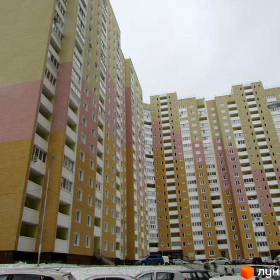 Високоповерховий будинок житлового комплексу Ярославичі з фасадом у жовто-рожевих тонах. На прибудинковій території припарковані автомобілі.