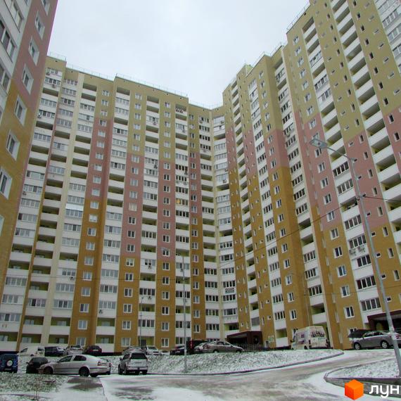 Високі багатоповерхові будинки ЖК Ярославичі з великою кількістю вікон та балконів. Біля будинків є парковка та прибудинкова територія з невеликим снігом.