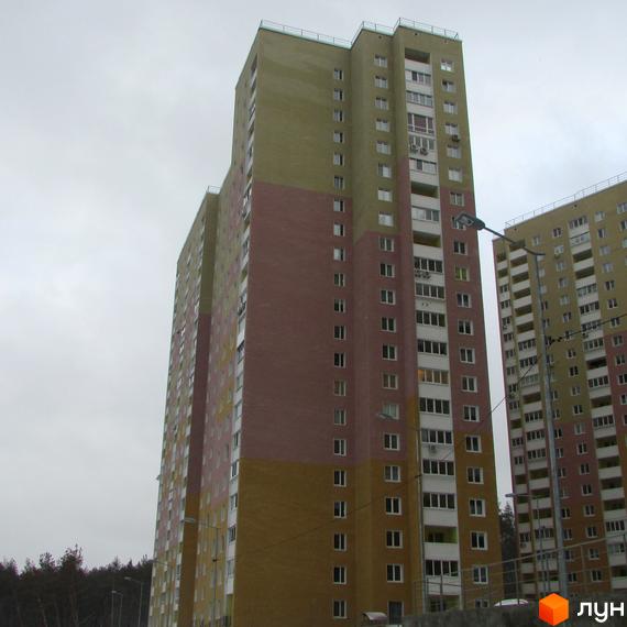 Високі багатоповерхові будинки житлового комплексу Ярославичі. На фото видно фасади будинків, виконані в різних кольорах. Навколо будівель є дерева та ліхтарі.